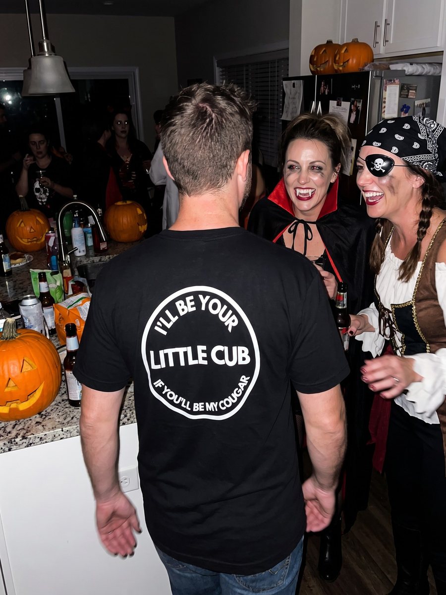 A vampire and a pirate reading the I'll Be Your Little Cub back print at a Halloween party